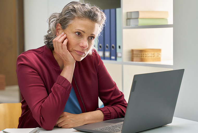 Eine Frau leidet unter den Folgen eines Vitamin-B12-Mangels und schaut nachdenklich in ihren Laptop.