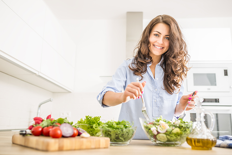 Eine junge Frau mit langen braunen Haaren bereitet Salate zu, während sie die Bedeutung der Vitamin-B12-Einnahme bei pflanzlicher Ernährung im Hinterkopf hat.
